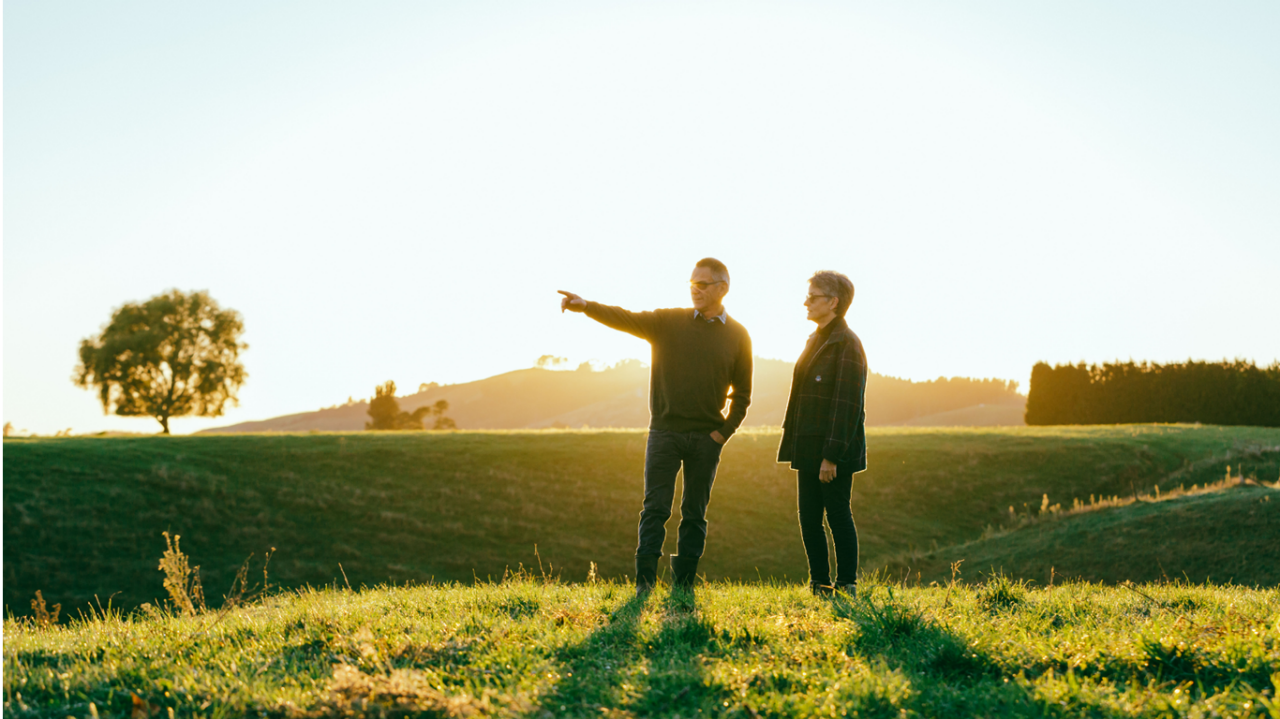 Male and female standing in field. Male pointing to something in the distance. 