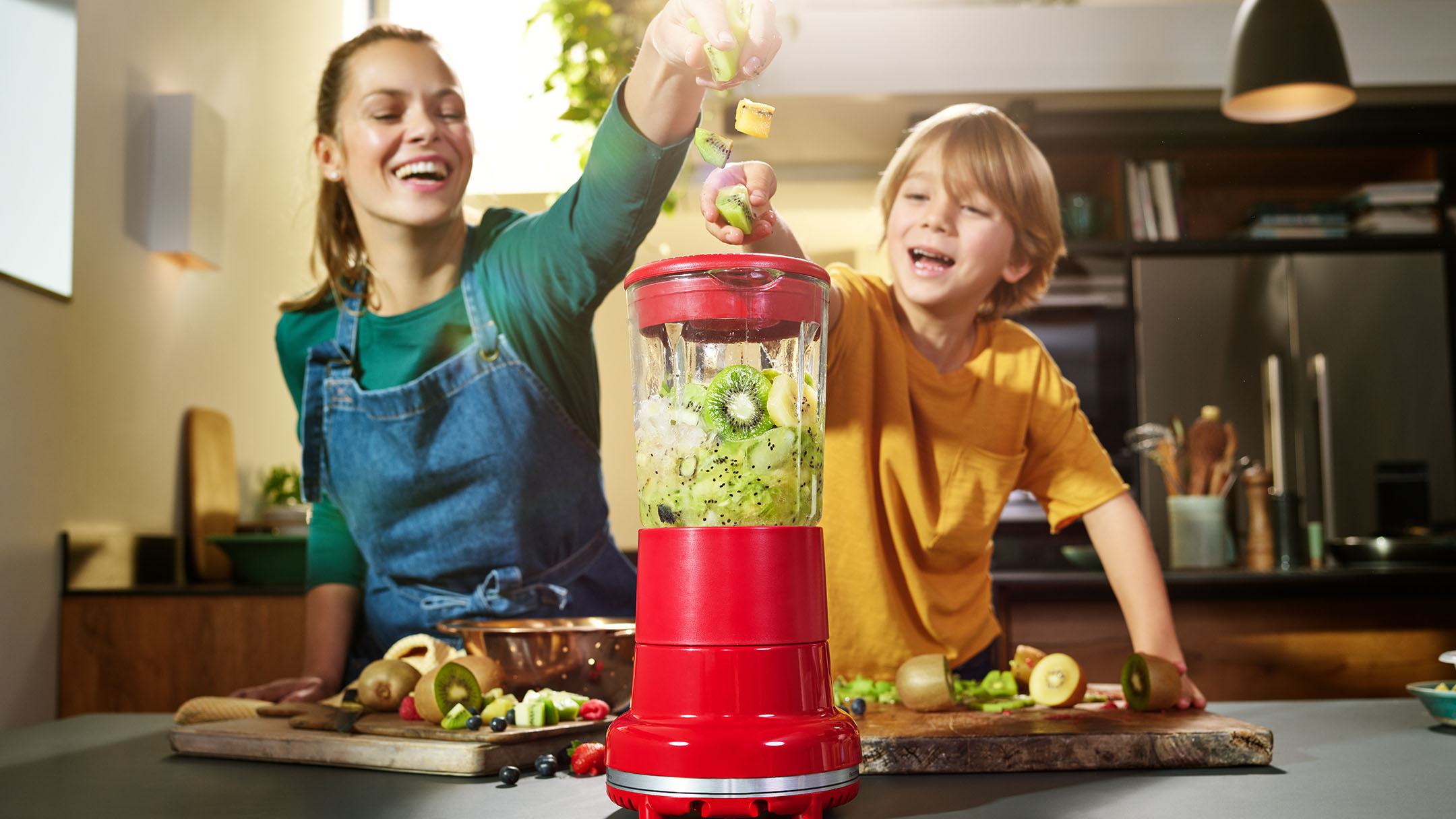 Mom and son blending green kiwi fruit smoothie in kitchen